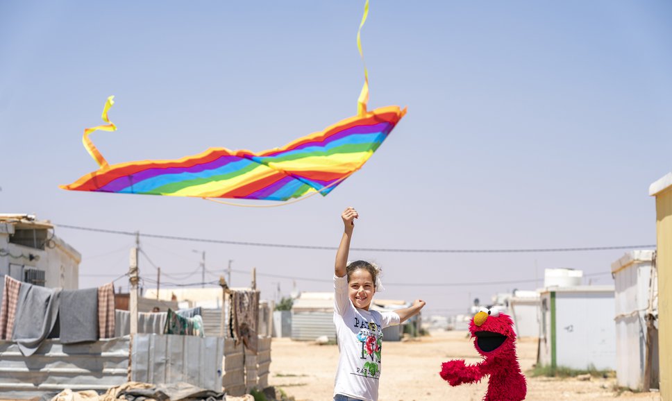 A friend shows Elmo how to fly a kite at Azraq Camp, Jordan.