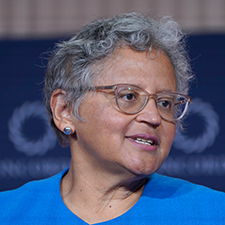 Cecilia Conrad looks off to the side during a panel discussion, wearing a blue shirt and glasses