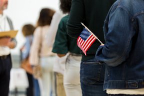 A person holds a small American flag while standing in line to vote