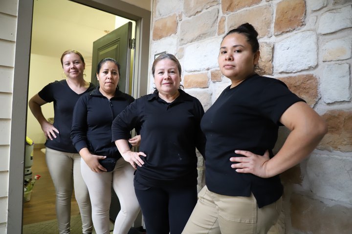 JUST team members stand against a brick wall in a doorway, wearing black t-shirts