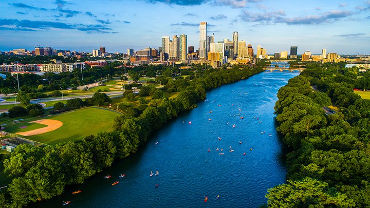 Aerial drone view above Lady Bird Lake showing kayakers on the water and the Austin, Texas skyline in the distance.