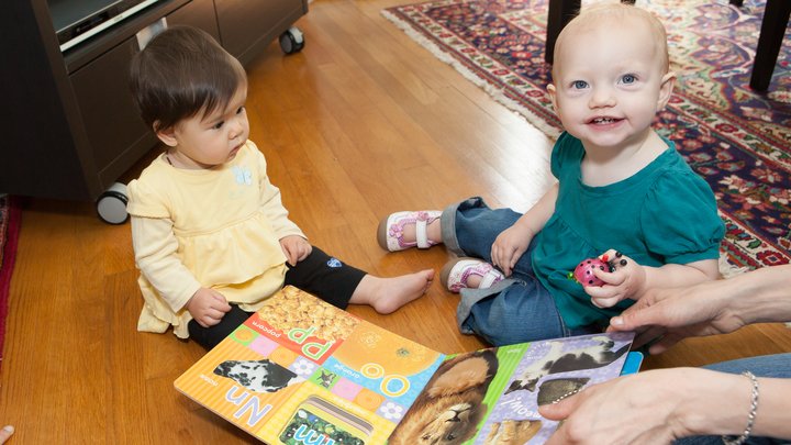 Two children sit on a hardwood floor playing with a book of the alphabet and a toy ladybug