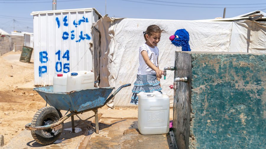 Ahlan Simsim’s Gargur helps a friend fetch water at Zaatari camp, Jordan.